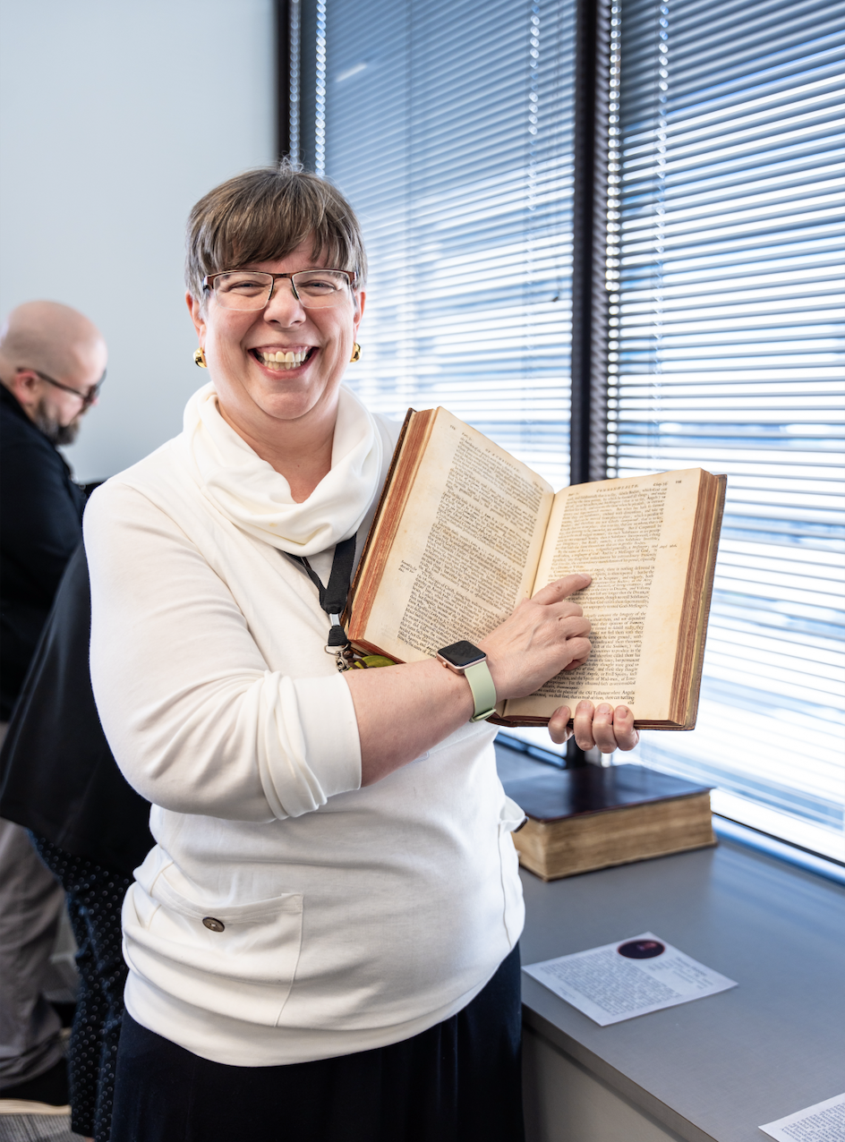 K-12 teacher smiling and point at a historical American book