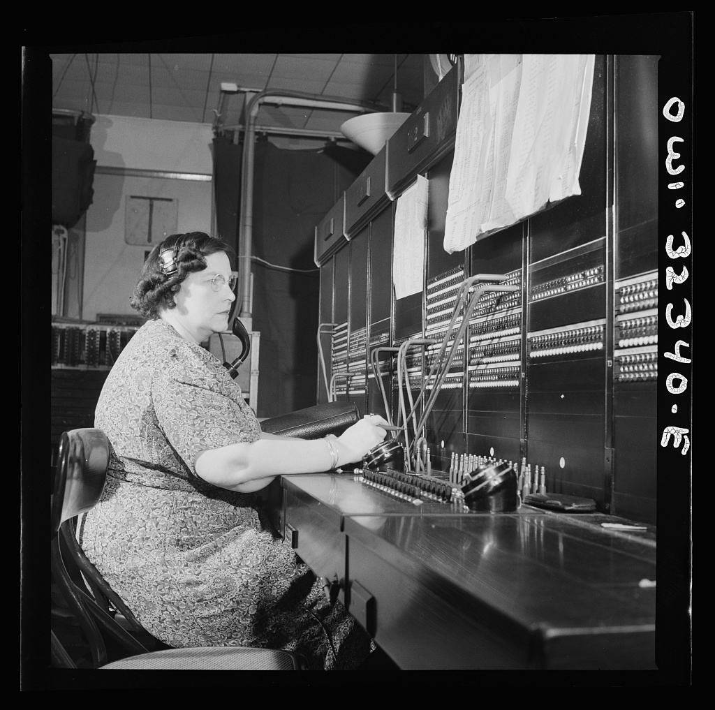Ethel Wakefield sits at a desk operating telegraph equipment.
